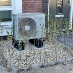 Unité extérieure de climatisation posée sur gravier devant une maison
