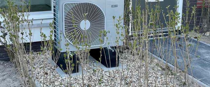 Unité extérieure de climatisation posée sur gravier devant une maison
