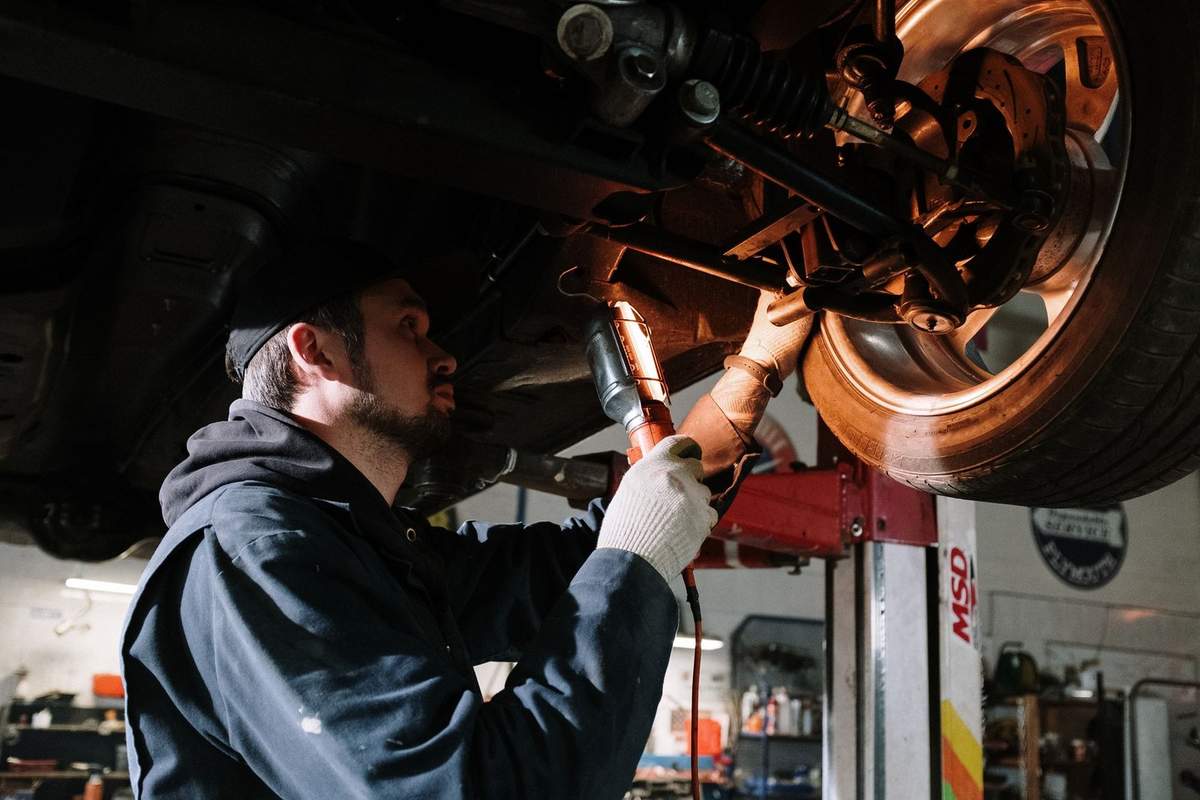 Mécanicien travaillant sur la suspension d'un véhicule soulevé dans un garage Mécanicien travaillant sur la suspension d'un véhicule soulevé dans un garage